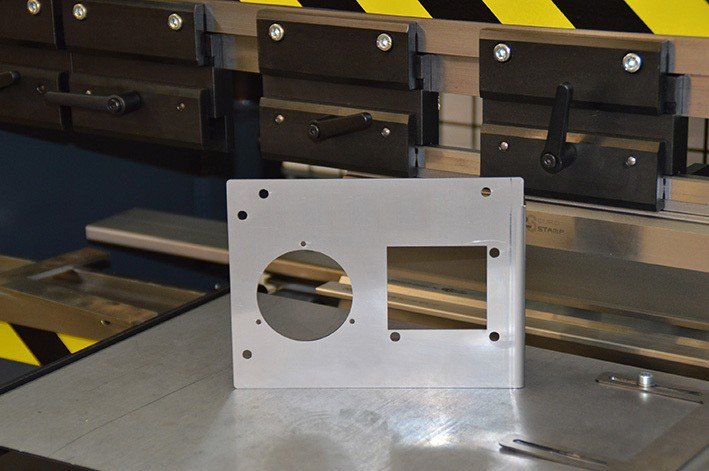 Metallplatte mit runder und rechteckiger Aussparung vor CNC-Abkantpresse – Beispiel für kombinierte Laser- und Kanttechnik