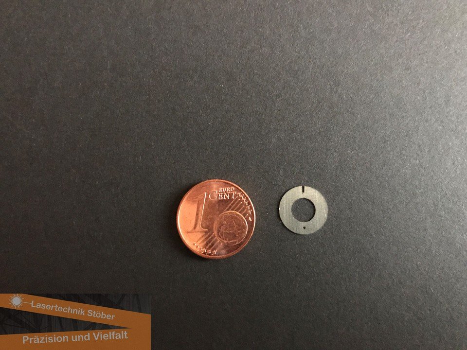 Kleines rundes Metallbauteil mit Nut neben einer 1-Cent-Münze auf dunklem Untergrund – Beispiel für Mikropräzision in der Laserfertigung