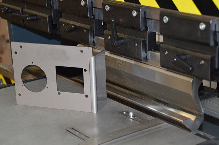Gebogenes Blechteil mit runder und rechteckiger Öffnung vor CNC-Abkantpresse – Beispiel für moderne Blechbearbeitung